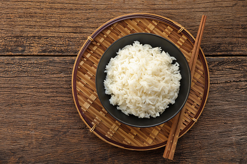 White rice in black bowl on a wooden background. Steam rice in black bowl on bamboo colander. empty space for text.