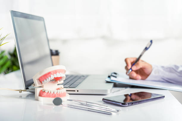 Médico dentista em uniforme escrevendo informações do paciente em lista de verificação de papelada na prancheta - foto de acervo