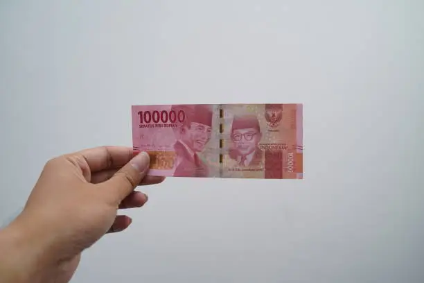 Photo of Hand holding one hundred thousand rupiah note isolated on white background. Indonesian rupiah currency