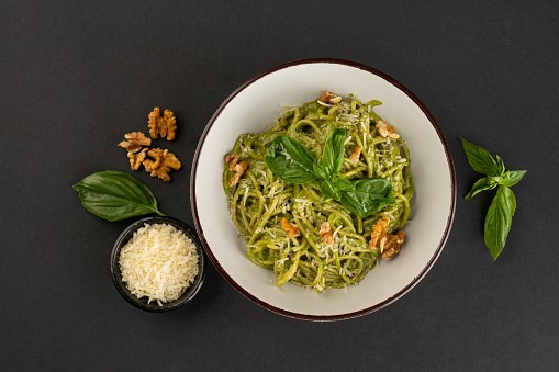 Pasta spaghetti with pesto sauce and fresh basil leaves in grey bowl. Dark grey background.Top view.