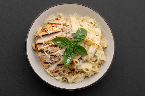 Chicken Alfredo Pasta in a Bowl Garnished with Basil Leaves shot on grey background