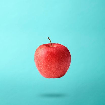 Red apple floating in mid-air, against light blue background with copy space.\nDiet concepts.