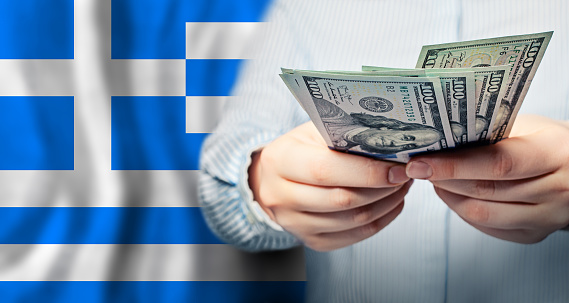 Hands with US dollars money on Greek flag background. Currency exchange, banking and business in Greece concept.