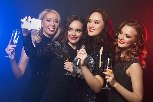 Group of partying women clinking flutes with sparkling wine and make selfie. Disco, party and people concept.