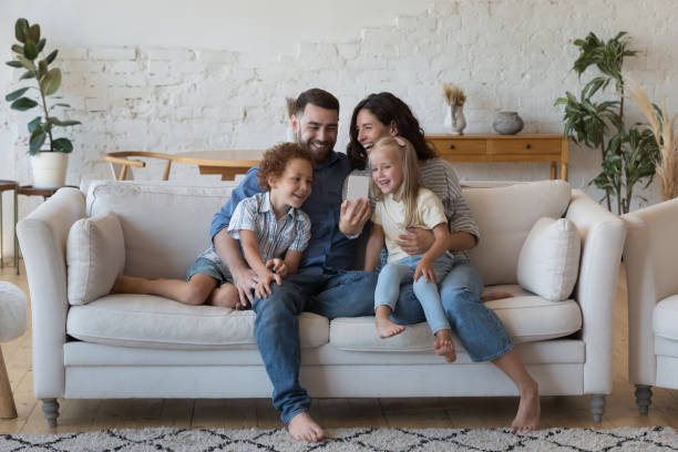 glückliche eltern, kleiner sohn und tochter, die sich per videoanruf unterhalten, - sofa stock-fotos und bilder