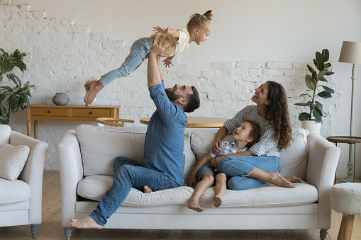 A family with three young boys is sitting on the sofa in their living room, photographed in high resolution with copy space