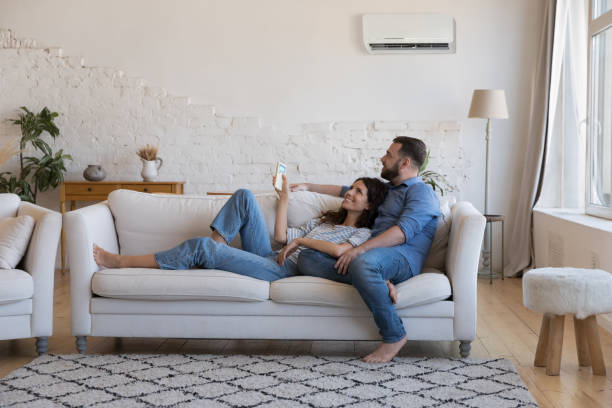 feliz pareja millennial de propietarios disfrutando de aire acondicionado fresco - sofá fotografías e imágenes de stock