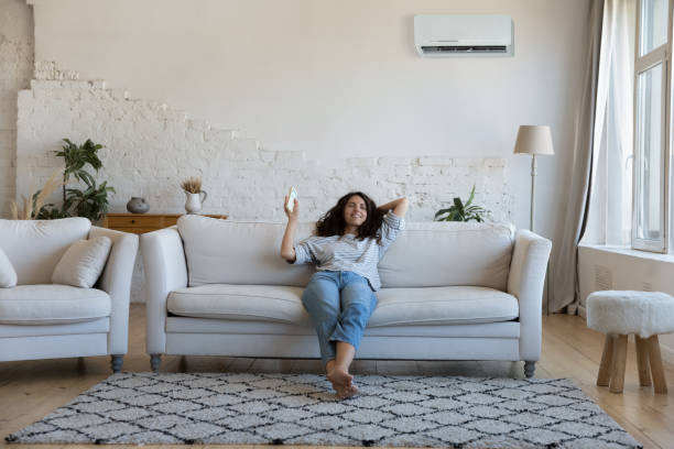 Happy pretty Latin woman enjoying cool conditioned air Happy pretty Latin woman enjoying cool conditioned air, relaxing on comfortable sofa, using remote control for turning AC on, starting cooling domestic equipment. Home appliance concept cool climate stock pictures, royalty-free photos & images