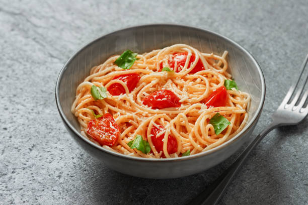 istock Spaghetti with cherry tomatoes and basil close-up on grey background from a high angle view indoors 1413559369
