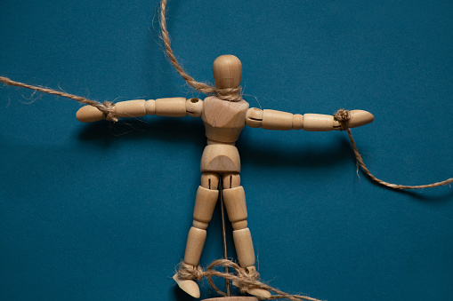 wooden man on ropes on an isolated background, tied to a man's hand, manipulation of people and slavery, free will, power over people