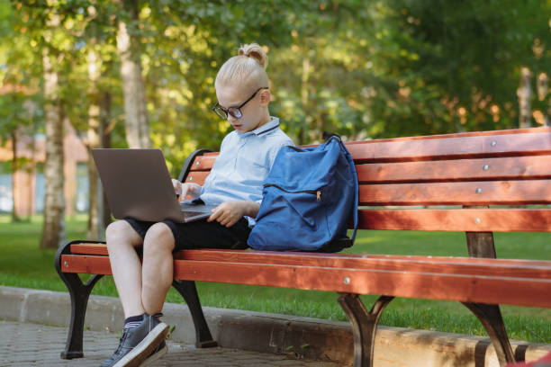 istock cute caucasian boy sitting on bench in park with laptop computer. Black screen 1413559422