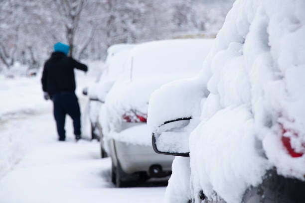 geparkte autos im schnee am morgen nach einem schneesturm, der fahrer reinigt den schnee von seinem auto, ukraine - schneesturm stock-fotos und bilder