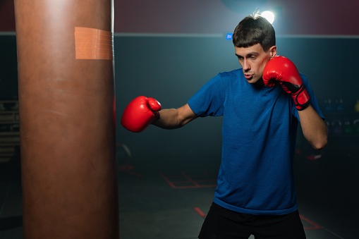 Photo of a young and handsome boxer with muscular build body with red gloves training in a gym