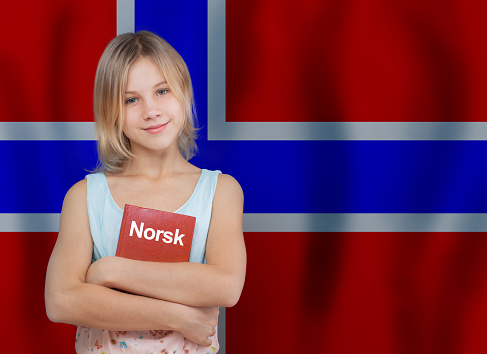 Cute little girl with textbook with inscription Norwegian in Norwegian language on flag of Norway background