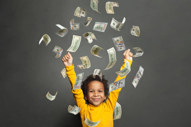улыбающийся маленький афроамериканский мальчик, стоящий с поднятыми руками под долларом сша, дождь на черном фоне - little boys black african descent american culture стоковые фото и изображения