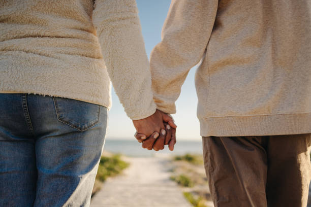 Romantic senior couple holding hands while walking down a boardwalk at the beach. Unrecognizable elderly couple taking a refreshing seaside holiday after retirement.