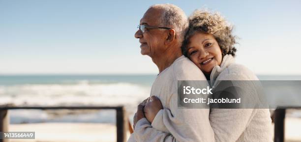Romantic Senior Woman Embracing Her Husband By The Ocean Stock Photo - Download Image Now