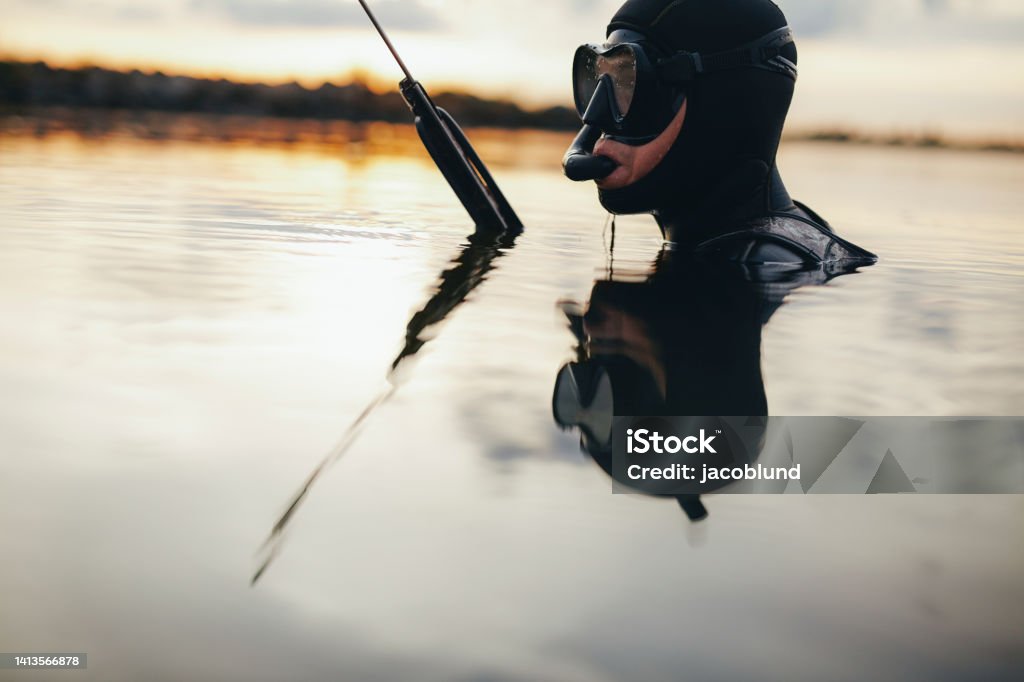 Spearfishing diver submerged in sea water Cropped shot of a spearfishing diver looking away while submerged in sea water. Fisherman hunting for fish using a speargun in the middle of the ocean. Underwater Stock Photo