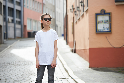 Child girl wearing white t-shirt with space for your logo or mock up outside in an urban area