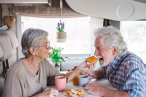 Beautiful happy caucasian senior couple in travel vacation leisure inside a camper van dinette enjoying breakfast together