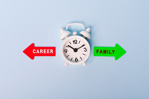 Career vs Family. Red arrow and green arrow- direction indicator - choice of Career or Family. Concept of choice. Two Arrows and White alarm clock on blue background, top view