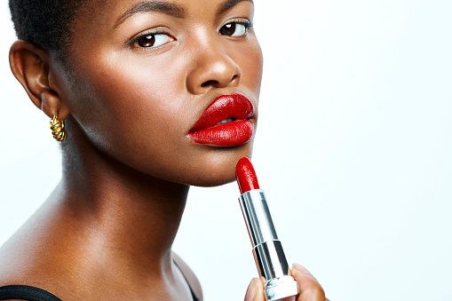 Beautiful African American model with red makeup and gorgeous skin, posing and looking into camera. Advertising skincare and cosmetics for ethnic women. Showing the latest shade of a popular lipstick
