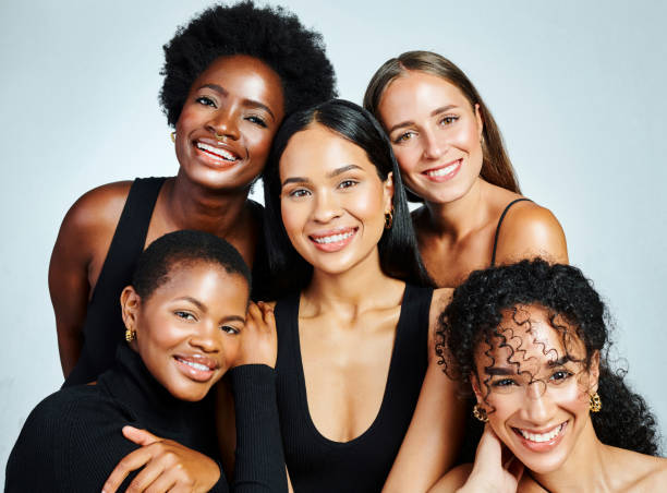 grupa różnorodnych i szczęśliwych kobiet pokazujących piękno, pielęgnację skóry i kosmetyki, pozując razem na szarym tle studyjnym. międzynarodowy portret kobiet z silnymi uśmiechami - stage makeup women beauty human face zdjęcia i obrazy z banku zdjęć
