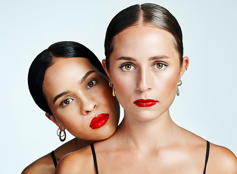 Two diverse, beautiful and stunning women standing and hugging against white studio background. Portrait of serious and gorgeous beauty models of different cultures and races with great skincare