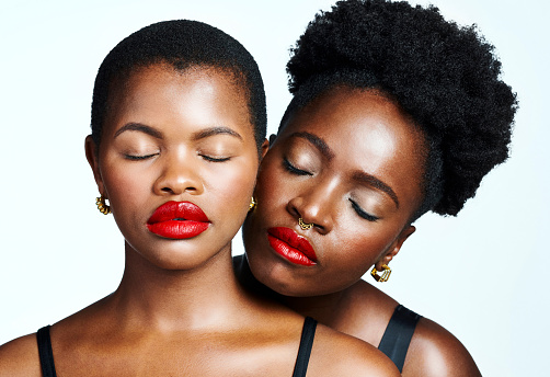 Two African American women with great skincare and makeup closed eyes standing together and hugging. Beautiful, stunning and attractive black natural beauty fashion models or girls with flawless skin