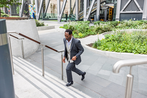 Mature South African businessman running upstairs outdoors in the city. He is running late for an important meeting.