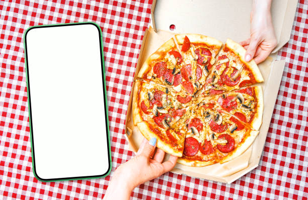 istock Pizza, hands and empty cellphone for your app design. Blank empty smartphone with white screen near the hands holding pizza slices. View above. 1413576438