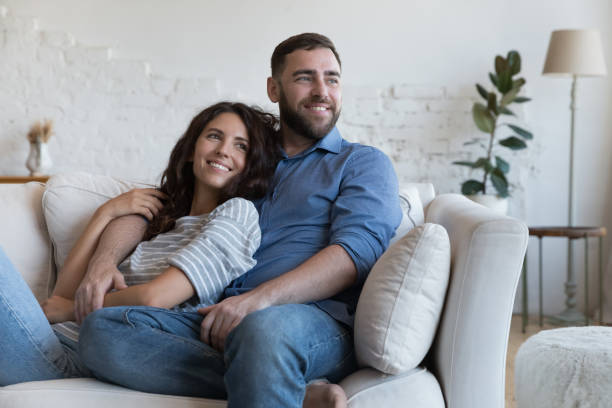 fröhliches, verträumtes junges dating-paar, das sich auf dem sofa ausruht - two parent family stock-fotos und bilder