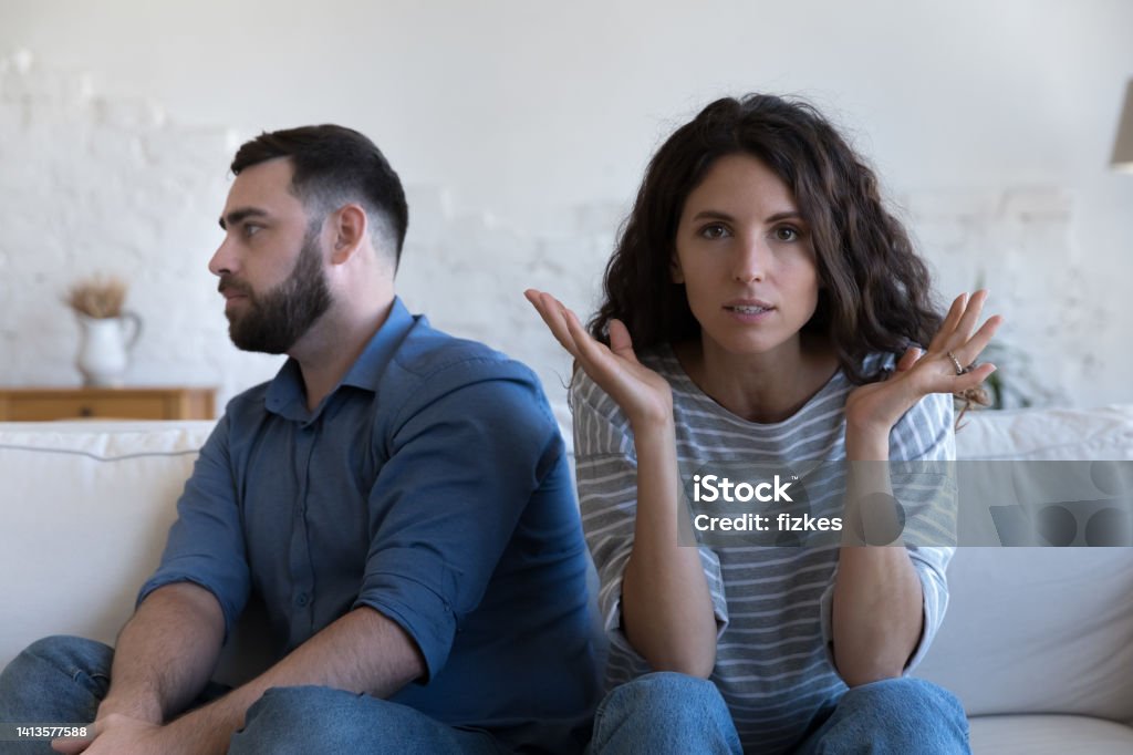 Annoyed married couple sitting on couch apart, after conflict, Annoyed married couple sitting on couch apart, after conflict, arguing, row. Serious angry wife looking at camera, tired husband turning away. Marriage crisis, counseling, relationships concept Couple - Relationship Stock Photo