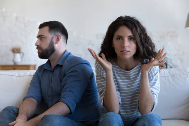 Annoyed married couple sitting on couch apart, after conflict, Annoyed married couple sitting on couch apart, after conflict, arguing, row. Serious angry wife looking at camera, tired husband turning away. Marriage crisis, counseling, relationships concept ignoring stock pictures, royalty-free photos & images