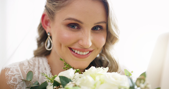 Happy, beautiful and stunning bride holding a bouquet and smiling at her white wedding. Portrait of a young gorgeous caucasian newlywed or wife at her ceremony or event with flowers