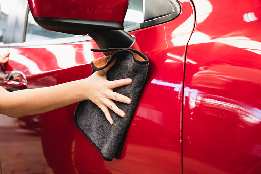 Woman dry wiping car surface with microfiber cloth after washing.