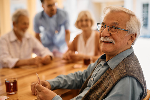 Happy senior man playing card with his friends at nursing home an looking at camera.