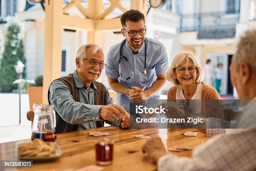 istock Happy seniors having fun while playing poker at nursing home. 1413581011