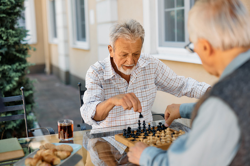 Senior man and his friend playing chess on patio at retirement community.