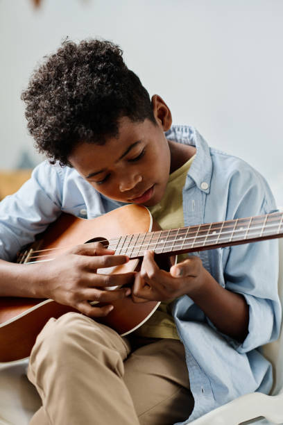 niño aprendiendo las notas en la guitarra - plucking an instrument fotografías e imágenes de stock