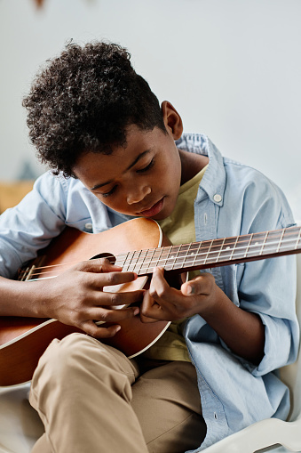 African boy examining the notes on guitar while he learning to play musical instrument at lesson