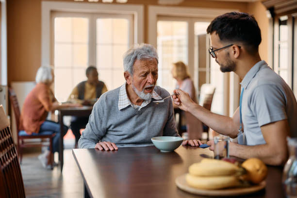 노인은 양로원에서 점심 시간에 간병인의 도움을 받아 식사를합니다. - senior adult nursing home eating home interior 뉴스 사진 이미지