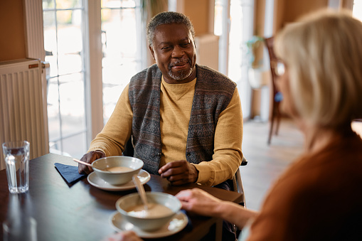 Happy seniors talking during lunch at dining table in nursing home. Focus is on African American man.