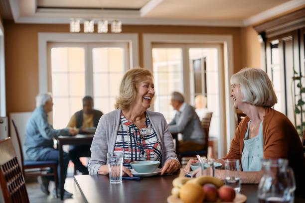 老人ホームで昼食をとりながら話している幸せな先輩女性。 - senior adult nursing home eating home interior ストックフォトと画像