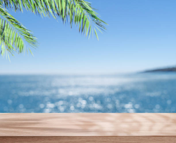 istock Empty table top under palm leaves and blurred sparkling sea at the background. Place for your product or brand name display. 1413583386