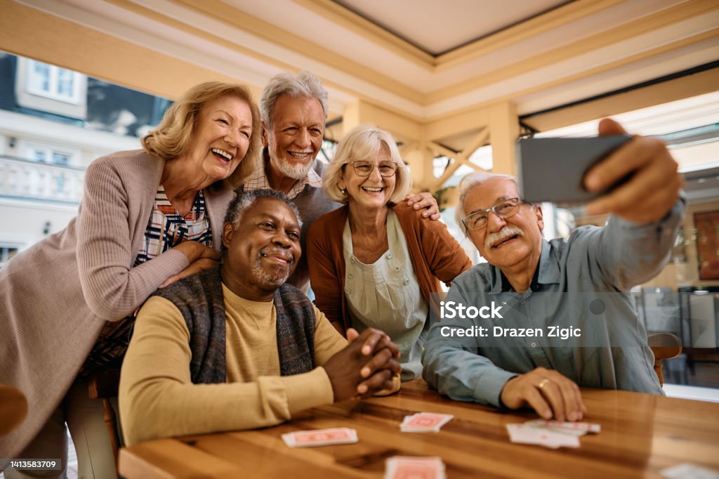 Cheerful senior having fun while taking selfie at retirement community. Multiracial group of happy senior people taking selfie with cell phone in nursing home. Senior Adult Stock Photo