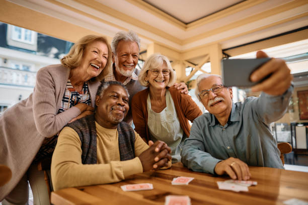 Cheerful senior having fun while taking selfie at retirement community. Multiracial group of happy senior people taking selfie with cell phone in nursing home. senior lifestyle stock pictures, royalty-free photos & images