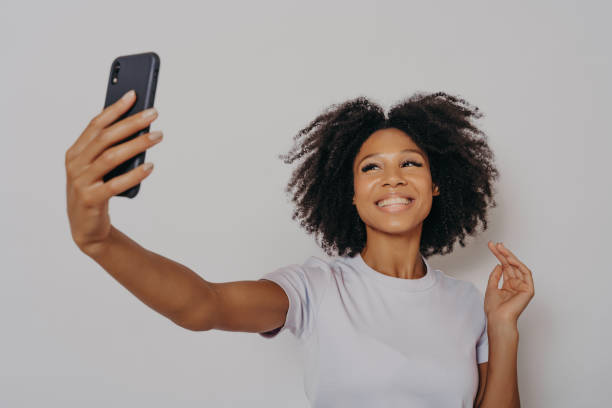istock Positive cheerful dark skinned female making photo on modern smartphone camera 1413583833