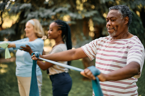 Black senior man using resistance band during exercise class in backyard of a nursing home.