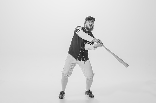 Practice in batting. Male baseball player wearing retro sports uniform and holding bat isolated on white background. Vintage baseball batter in action. Concept of sport, fashion, emotions, ad